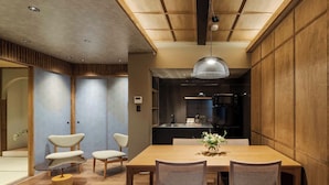 Un comedor moderno con una mesa de madera, cuatro sillas, una lámpara colgante y una cocina al fondo.