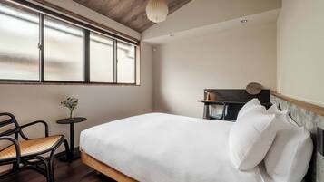 A bedroom with a bed, a chair, a small table with a vase, and a window with frosted glass.