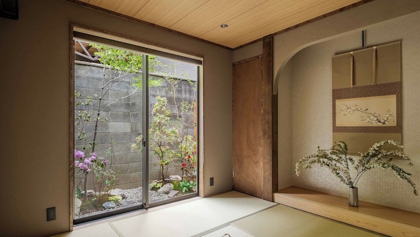 Una habitación tradicional japonesa con suelo de tatami, una puerta corrediza que da a un jardín y techo de madera.