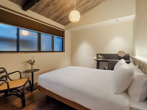Ein Schlafzimmer mit Bett, Stuhl, kleinem Tisch, Schreibtisch und Fenster mit Jalousien.
