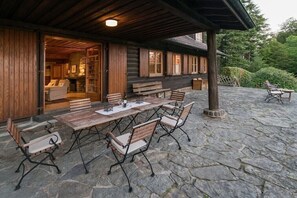 A covered outdoor patio with stone flooring, wooden tables and chairs, and a stone fireplace. - Gommerscheid Hunting Lodge (Ehlscheid)