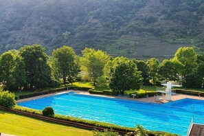 Ein Schwimmbecken mit Sprungbrett, umgeben von üppiger Vegetation und Hügeln im Hintergrund.