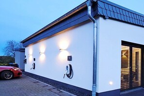 Un bâtiment moderne à l’extérieur blanc, avec une porte de garage et une voiture rouge garée devant.