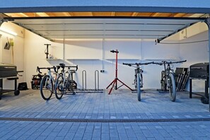 Eine Garage mit Fahrrädern, einem Motorrad, einem roten Tisch und einer Werkbank.