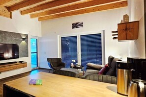 Un salon moderne avec un plafond en bois, un téléviseur à écran plat, un canapé, une table basse et une fenêtre avec des stores.