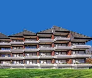 Ein mehrstöckiges Hotel mit Balkonen, einer flachen Dachterrasse und einem gepflegten Rasen.