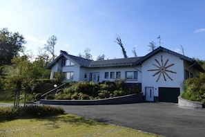 A modern two-story house with a large sunburst mural on the side, a garage, and a well-maintained lawn. - Villa in Schmallenberg with swimming pool (Schmallenberg)