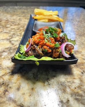 A dish of grilled meat with vegetables and a side of fries on a marble countertop.