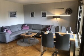 Ein modernes Wohnzimmer mit einem grauen Sofa, einem Holztisch und einem Essbereich mit Stühlen und einem Tisch.