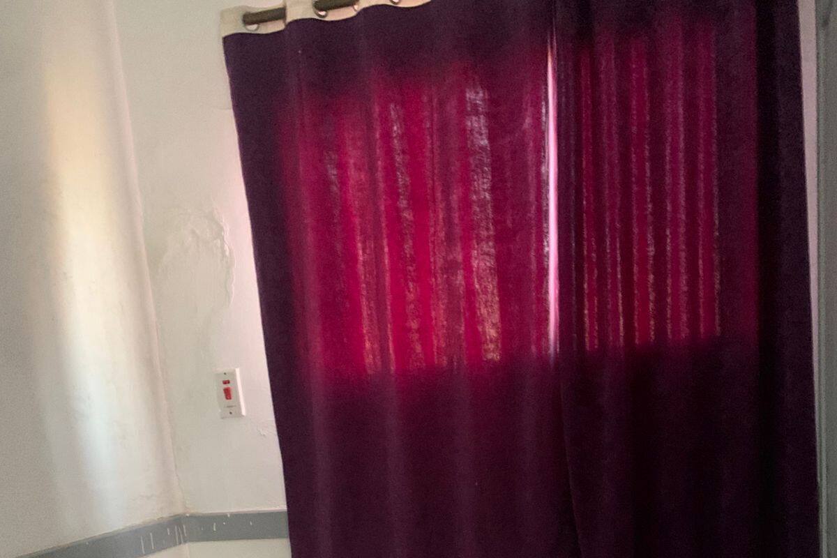 A single bed with a white mattress and a striped blanket, a small table, and a purple curtain.