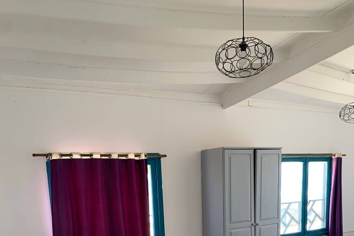 A bedroom with a bed, a wardrobe, a nightstand, a window with curtains, and a hanging light fixture.