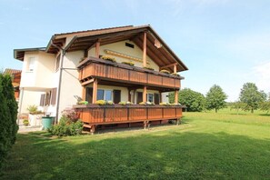 Ein zweistöckiges Gebäude mit einem Holzbalkon, einem geneigten Dach und einem Garten davor.