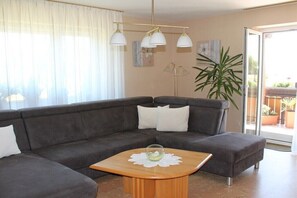 Ein Wohnzimmer mit einem Ecksofa, einem Holztisch und einer großen Topfpflanze.
