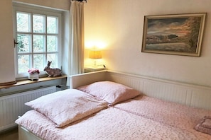 Ein Schlafzimmer mit einem Bett, einem Fenster mit Vorhängen, einer Lampe und einem Bild an der Wand.