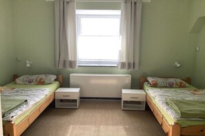 Ein Zimmer mit zwei Einzelbetten, einem Heizkörper, einem Fenster mit Vorhängen und Nachttischen.