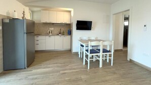 A modern kitchen with a refrigerator, cabinets, and a dining area with chairs. - Apartments Vicelić (Orebic)