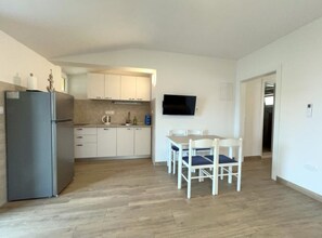 A modern kitchen with a refrigerator, cabinets, and a dining area with chairs. - Apartments Vicelić (Orebic)