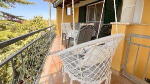 A balcony with wicker chairs, a table, and a view of greenery. - Apartments Vicelić (Orebic)