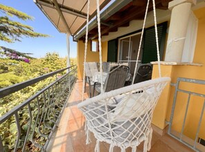 A balcony with wicker chairs, a table, and a view of greenery. - Apartments Vicelić (Orebic)