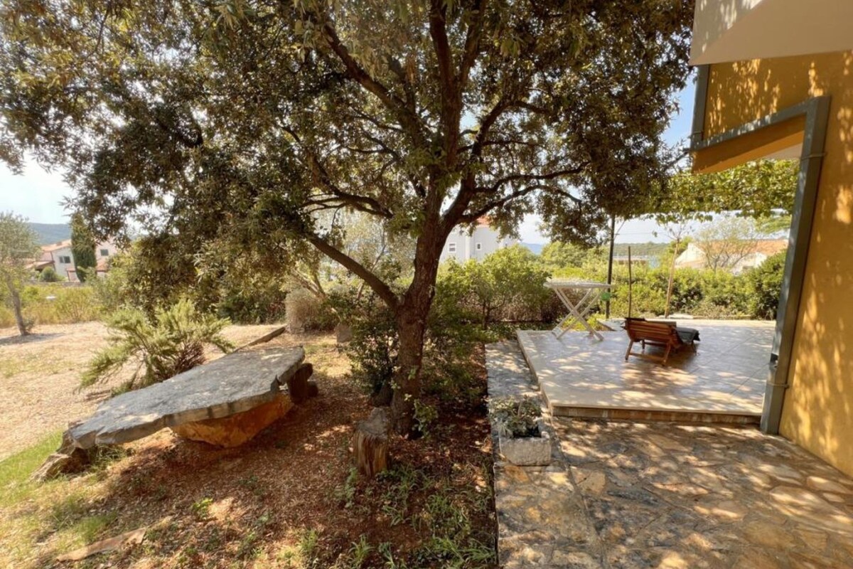 A stone patio with a bench, a tree, and a view of the sea.