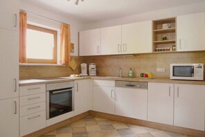 Una cocina con armarios blancos, microondas, cafetera y ventana con cortinas.