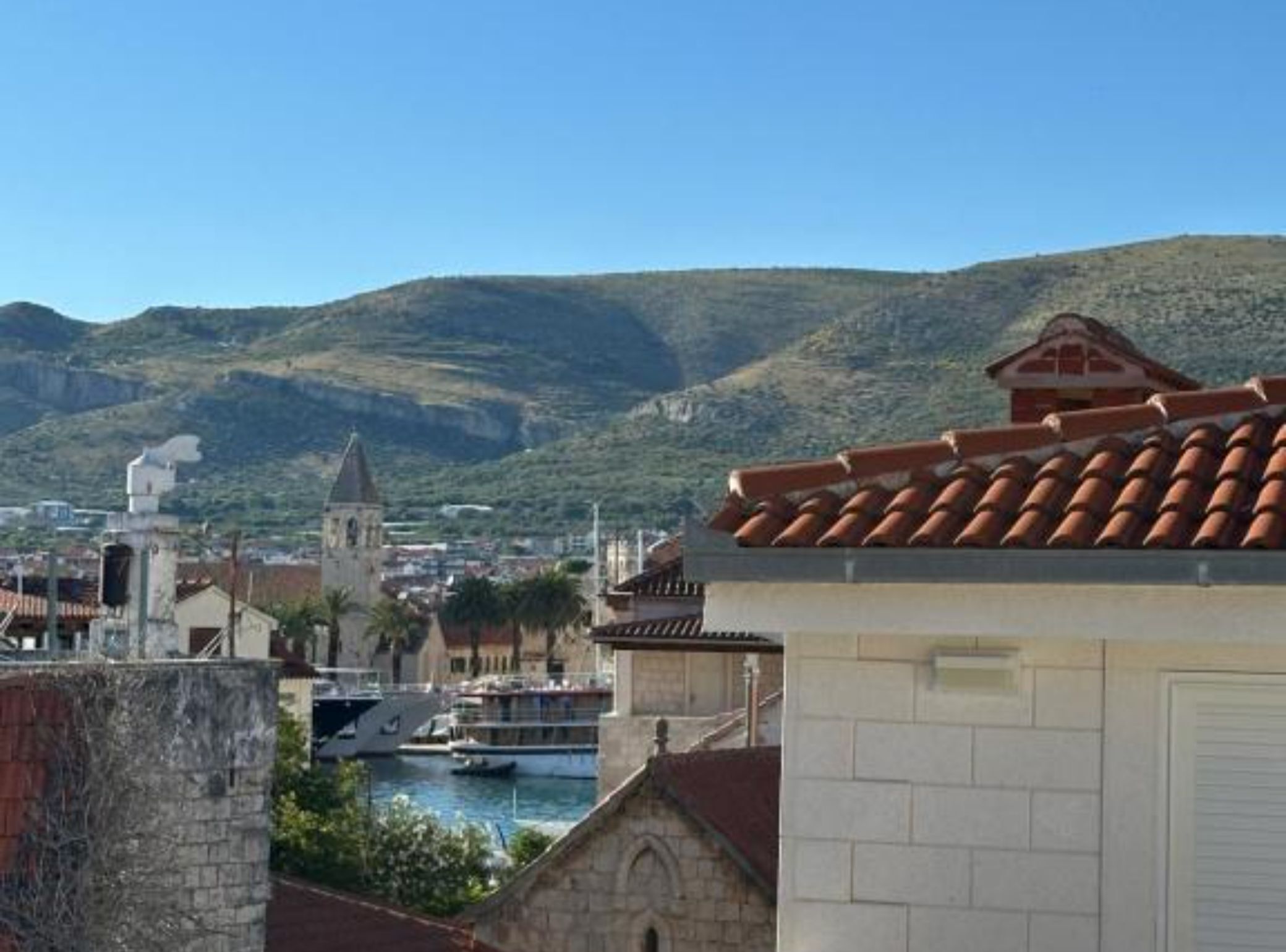 Un pueblo costero con una iglesia, un puerto lleno de barcos y montañas al fondo.