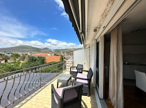Un balcón con mobiliario de mimbre, vistas a la ciudad y una montaña al fondo.