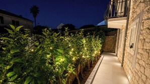 Un sendero bordeado de plantas iluminadas que conduce a un edificio de piedra con balcón.