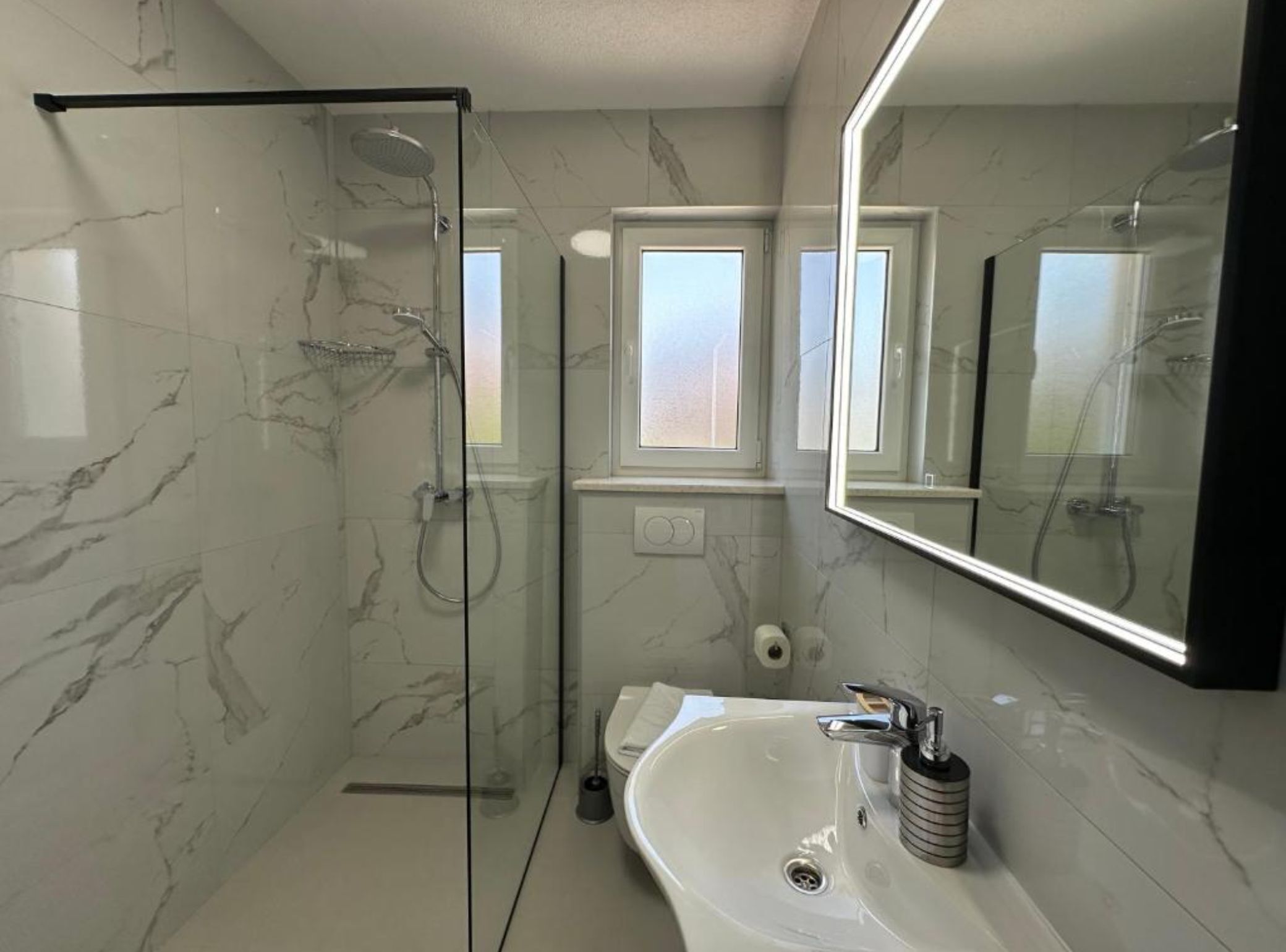 Un baño moderno con ducha de vidrio, un lavamanos grande de color blanco y un espejo sobre el lavamanos.