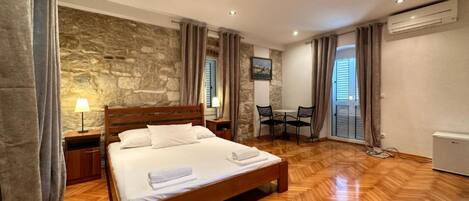 A bedroom with a wooden bed, stone wall, and a dining area with a table and chairs.
