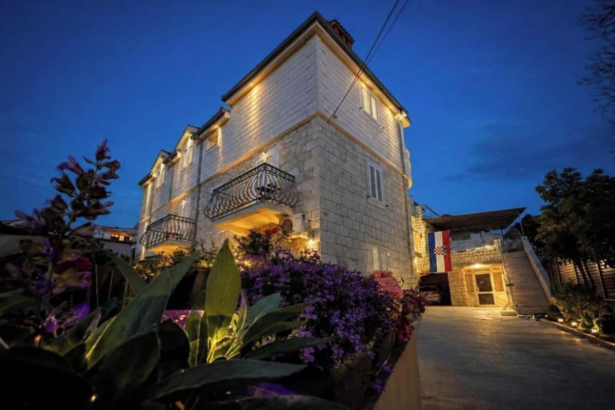 A two-story building with a balcony, surrounded by flowering plants.
