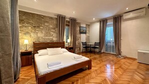 A bedroom with a wooden bed, stone wall, and a dining area with a table and chairs. - Villa Dante (Trogir)