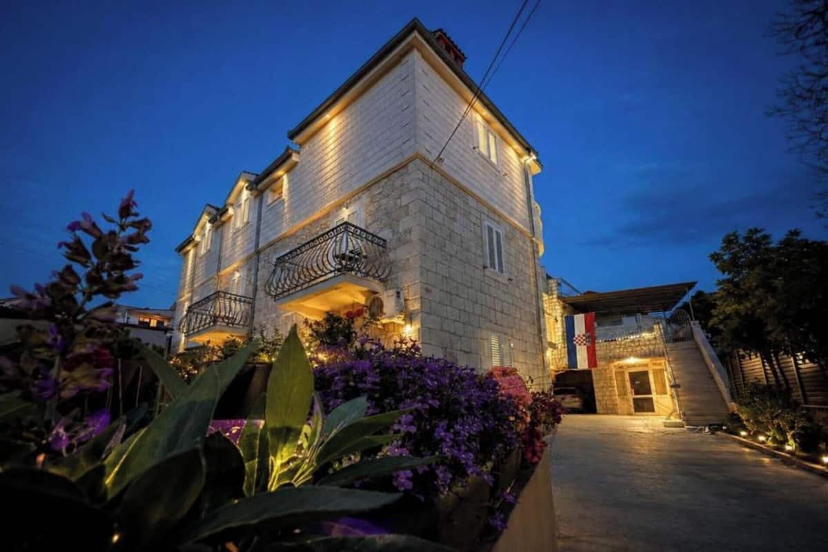 A two-story building with a balcony, surrounded by flowering plants.