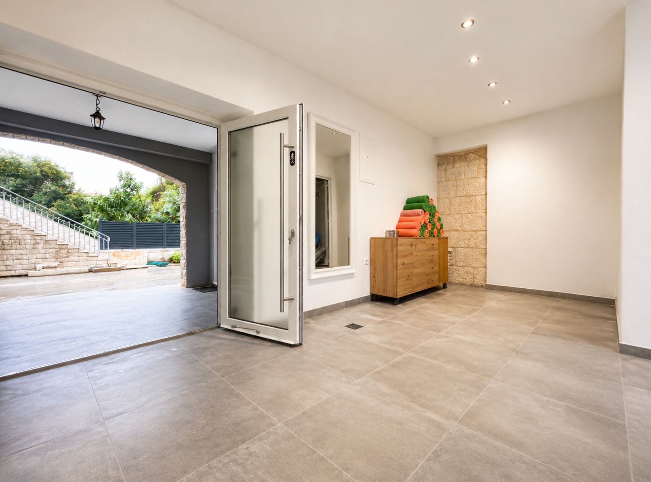 A modern interior with a glass door leading to an outdoor area, a wooden cabinet with folded towels, and a staircase.