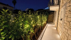 A pathway lined with illuminated plants leading to a stone building with a balcony. - Villa Dante (Trogir)