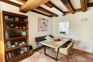 A dining area with a wooden table, chairs, a bookshelf, a painting, a clock, and a window with blinds. - Holiday home with 2 bedrooms (Mainz-Kostheim)