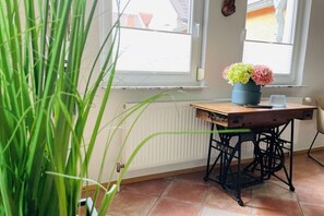 A room with a radiator, a window with blinds, a wooden table with a vase of flowers, and a chair. - Holiday home with 2 bedrooms (Mainz-Kostheim)