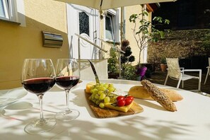 Ein Tisch mit zwei Gläsern Rotwein, einer Käseplatte mit Trauben und Tomaten sowie einem Brot.