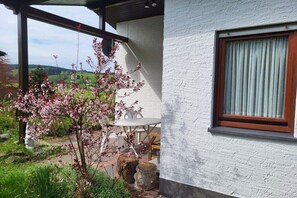 A white building with a window, a wooden table, and a chair outside. - Holiday home with 2 bedrooms (Olsberg- Bruchhausen)