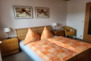 A bedroom with a bed, two pillows, a nightstand, a chair, and two wall-mounted lamps. - Holiday home with 2 bedrooms (Olsberg- Bruchhausen)