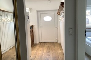 Ein Flur mit Holzboden, einer weißen Tür mit rundem Fenster und einem Kleiderständer.