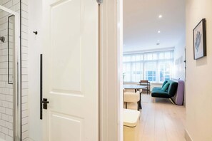 A modern interior with a white door, a dining area with a table and chairs, and a green sofa. - Chic 1BDR Retreat in St Johns Wood (Greater London)