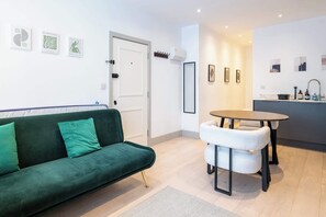 A modern living room with a green sofa, a white chair, a small round table, and a kitchen area with a sink and countertop. - Chic 1BDR Retreat in St Johns Wood (Greater London)
