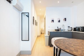 A modern kitchen with a dining area, featuring a built-in stove, sink, and a wooden dining table. - Chic 1BDR Retreat in St Johns Wood (Greater London)