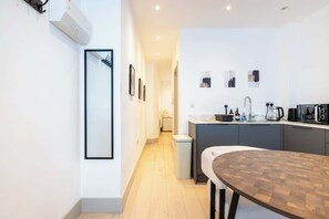 A modern kitchen with a dining area, a small trash bin, and a hallway leading to a bathroom. - Chic 1BDR Retreat in St Johns Wood (Greater London)
