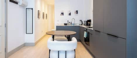 A modern kitchen with a round table, white chairs, and a grey refrigerator.