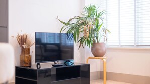 Ett modernt vardagsrum med en svart möbel för underhållningssystemet, en platt-TV, en krukväxt och en liten träpall.