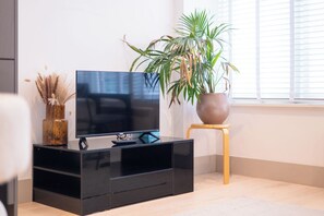 A modern living room with a black entertainment unit, a flat-screen TV, a potted plant, and a small wooden stool. - Chic 1BDR Retreat in St Johns Wood (Greater London)