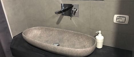 A modern bathroom with a stone sink, a black countertop, a mirror, and a wall-mounted light.