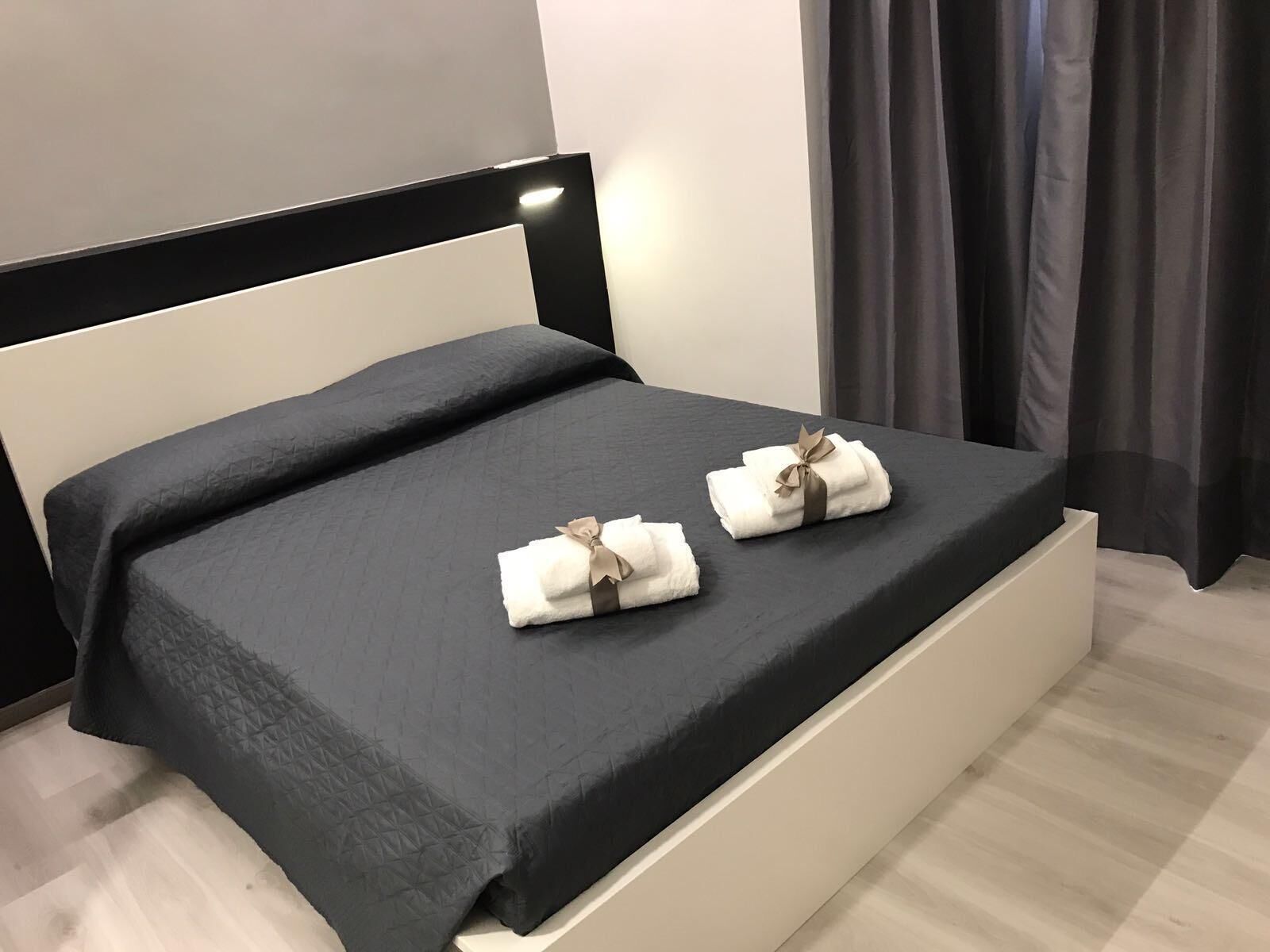 A bed with a black mattress and white headboard, two towels with bows, and a light-colored wall.